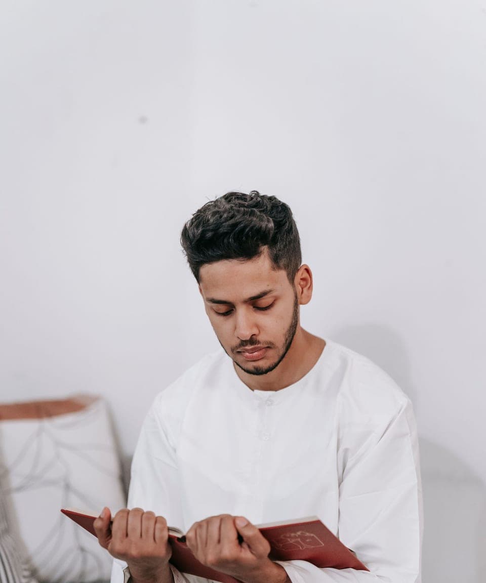 A young man in a white thobe reading the Quran