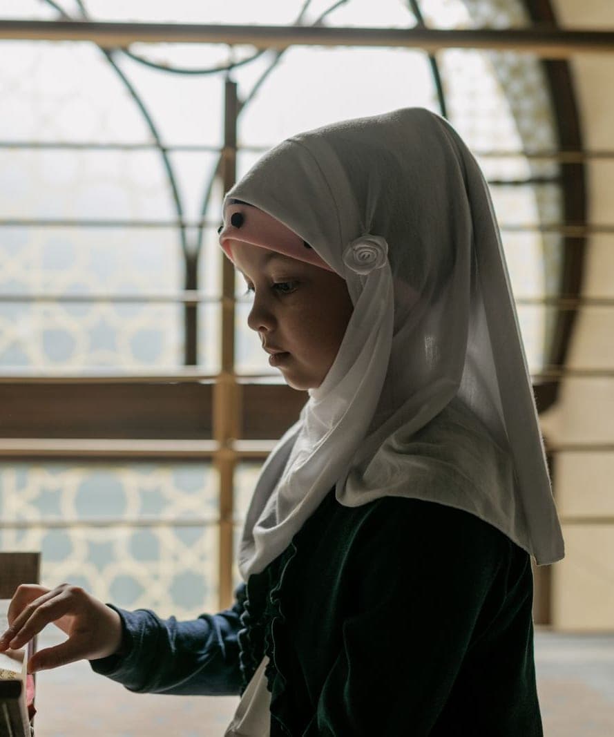 A young girl in a hijab reading the Quran at a wooden stand
