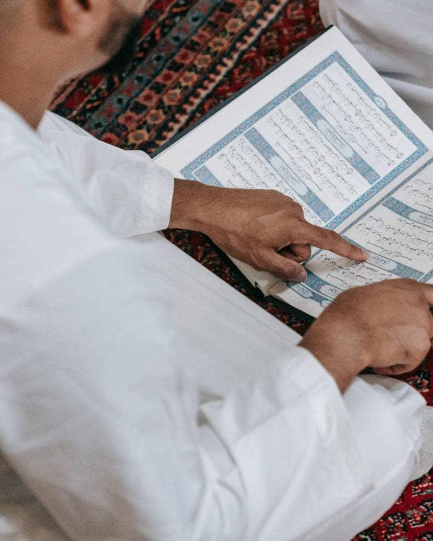 A teacher pointing to the line a student is reading in the Quran