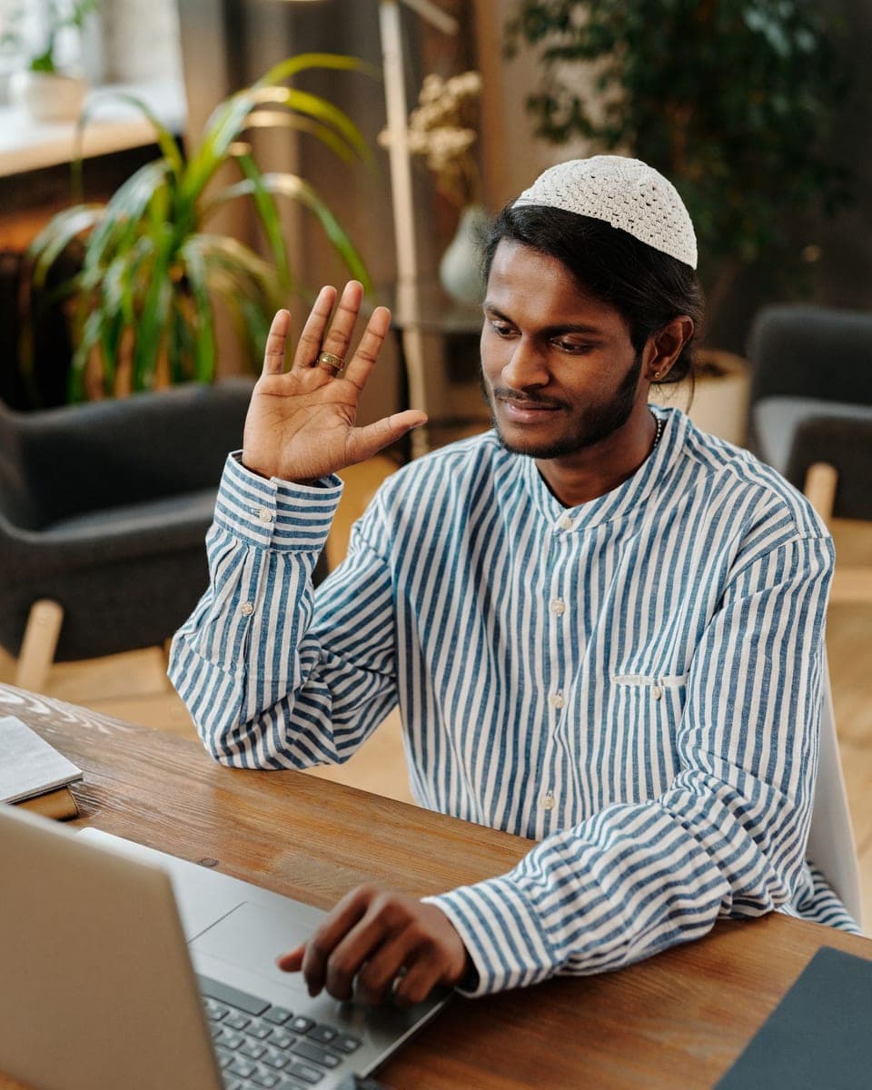 A man in a kufi waving at the start of a video lesson on his laptop